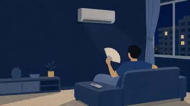 A person fanning themselves on a sofa at night under a running aircon