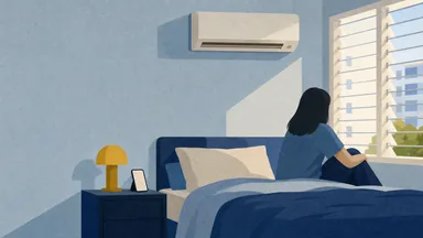 A phone on a bedside table under a wall aircon in a sunlit bedroom